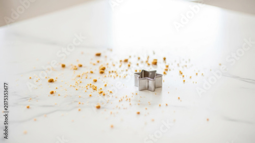 Metal star shaped cookie cutter surrounded by brown sugar crumbs on a clean white marble countertop surface for holiday baking