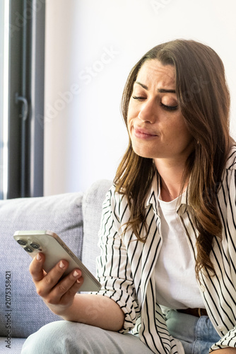 Картината върху платно Young woman on couch looking skeptically at her smartphone, reacting to a messag