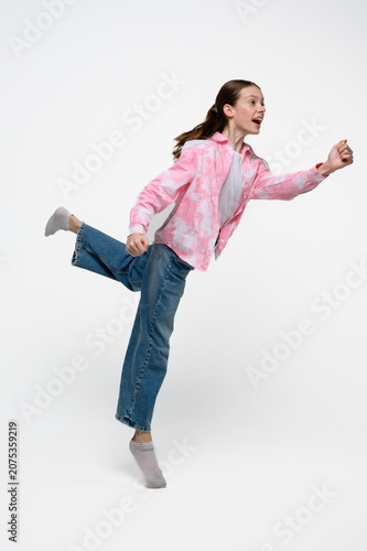Happy teenage girl running with a cheerful smile. Studio portrait expressing energy, movement, freedom, playfulness and active lifestyle.