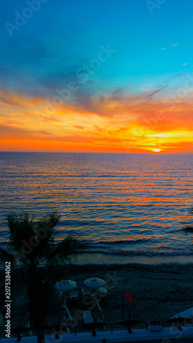 A breathtaking panoramic view of a dramatic golden sunset over the Mediterranean Sea in Agropoli, Cilento coast. The sky is filled with vibrant hues of orange, pink, yellow, and blue clouds, while the