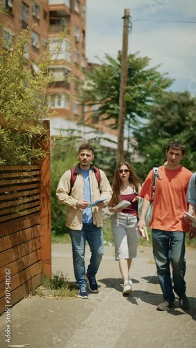 A diverse group of young students walks casually outdoors. Friends enjoy a conversation while strolling on a sunny campus.