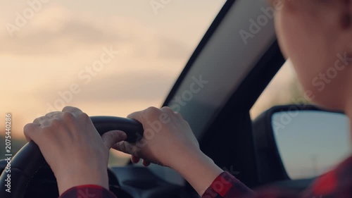 Woman is driving a car with her hands on the steering wheel. The sun is setting, casting a warm glow on the scene