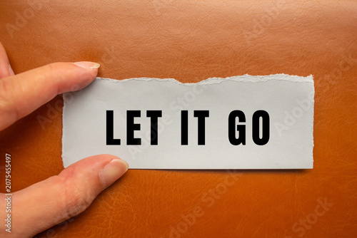 Fotografie Hand holding a ripped paper with the words let it go on a brown background, symb
