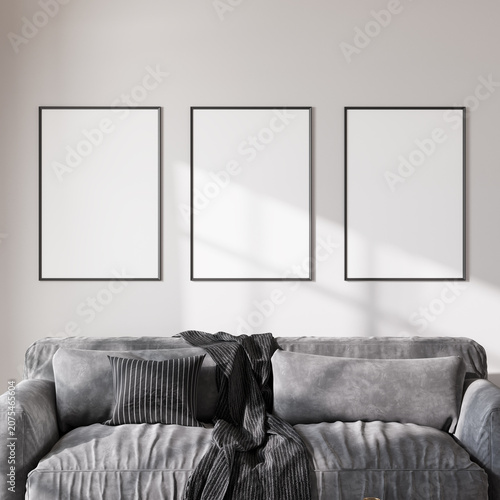 Three blank poster frames mockup on living room wall above grey sofa, 3d render