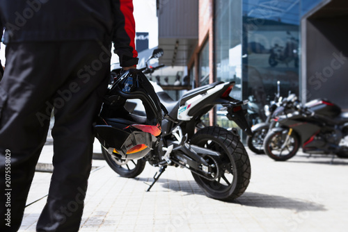 Motorcycle rider holding helmet near modern bikes outside showroom in urban lifestyle scene