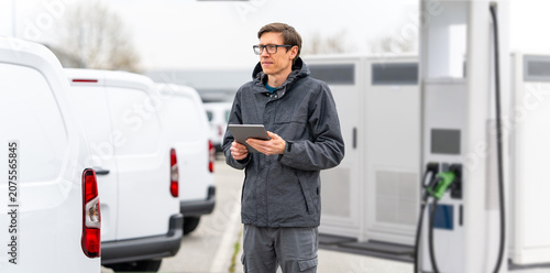 Fleet manager with digital tablet supervising rows of white electric delivery vans
