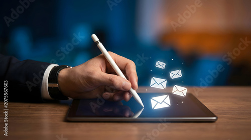 Hand using stylus on tablet with glowing email icons floating above message