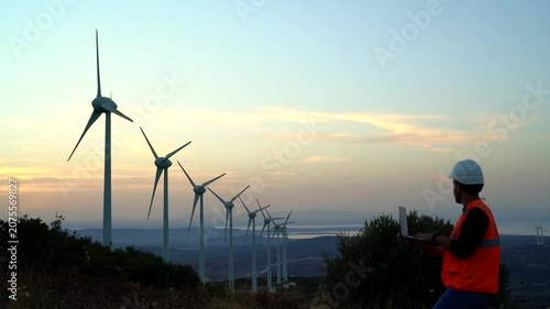 Wind turbine technician inspecting equipment at a renewable energy farm during sunset