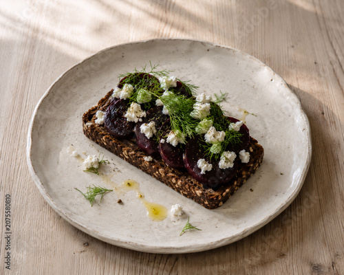 Artisan open faced toast topped with roasted beetroot slices, creamy feta cheese, fresh dill, and olive oil, served on rustic whole grain bread. A healthy gourmet dish presented on a ceramic plate.