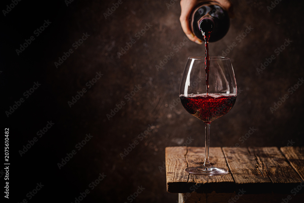 Fototapeta premium Pouring red wine into the glass against rustic dark wooden background