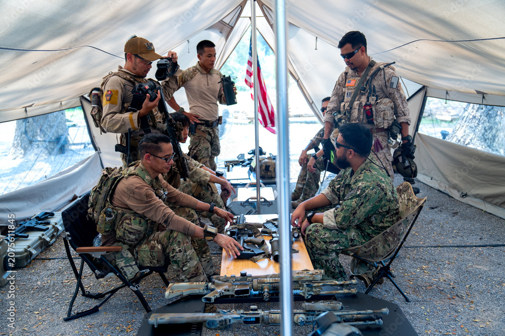 Fototapeta premium Group of army with different types of equipment and weapons have meeting and plan inside field tent.