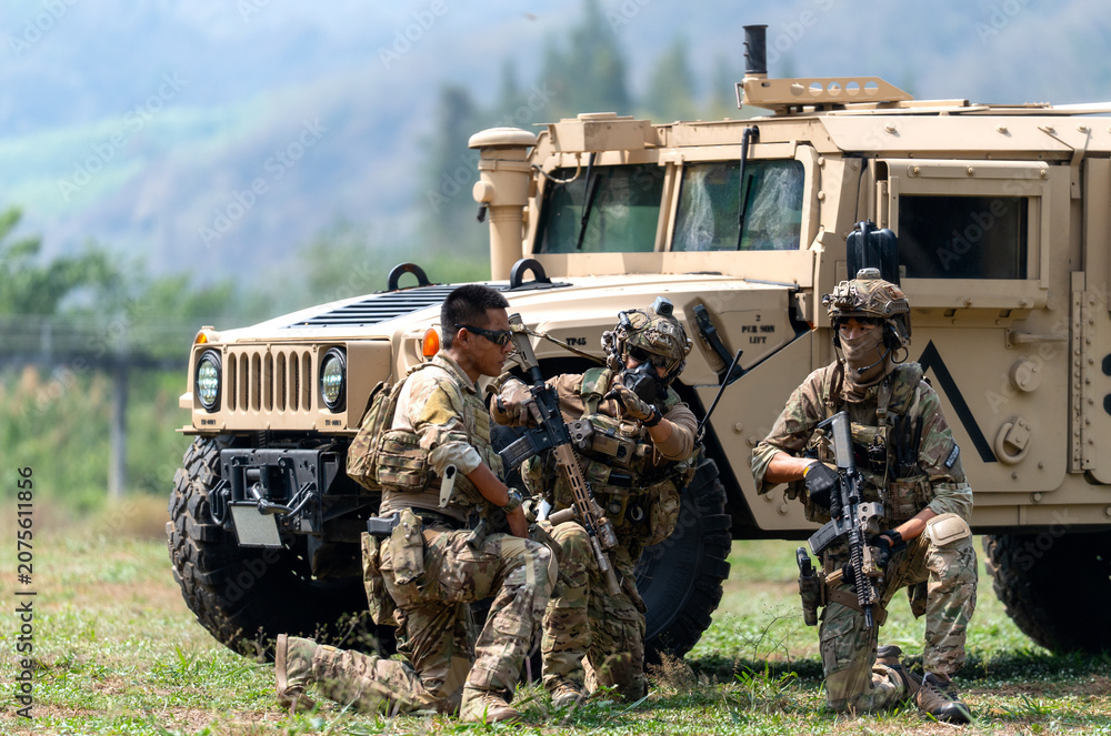 Fototapeta premium Three military men sit beside High Mobility Multipurpose Wheeled Vehicle and discuss about plan to fight the enemy with day light.
