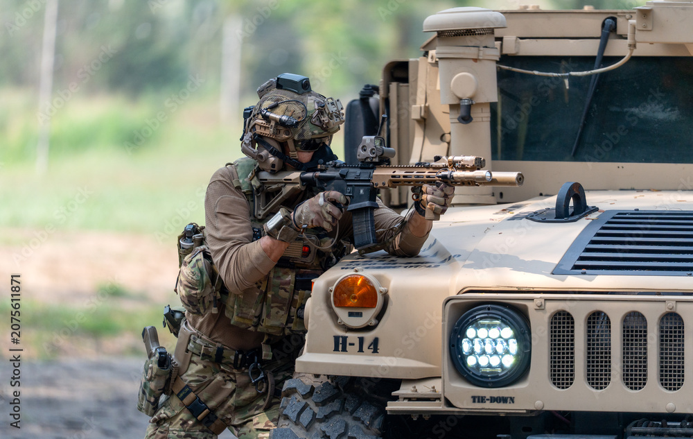 Fototapeta premium One army man point gun to enemy direction and lean on front hood of High Mobility Multipurpose Wheeled Vehicle to practice of fight with enemy.