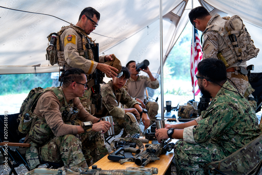 Fototapeta premium Close up shot group of army with different types of equipment and weapons have meeting and plan inside field tent.