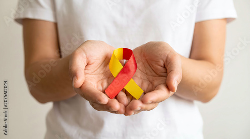 Red and yellow awareness ribbon held in hands, hepatitis C and world hepatitis day concept, medical health support symbol in palms
