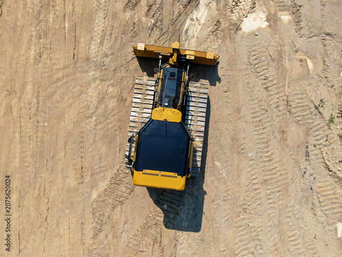 Top Down Aerial View Of Yellow Bulldozer Crawler Tractor On Graded Dirt Staging Area