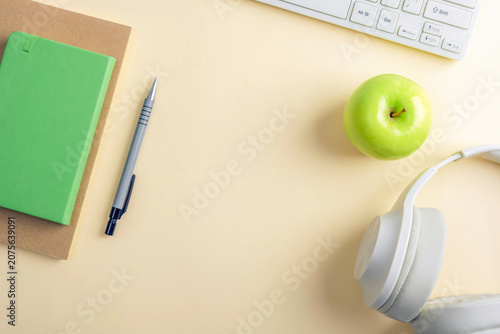 Minimalist workspace with notebook, pen, keyboard, headphones and green apple on a beige desk. Top view, flat lay, copy space