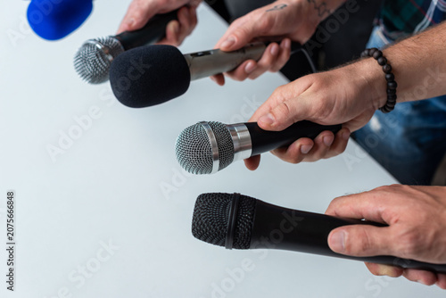 Hands holding various microphones, ready for an interview.