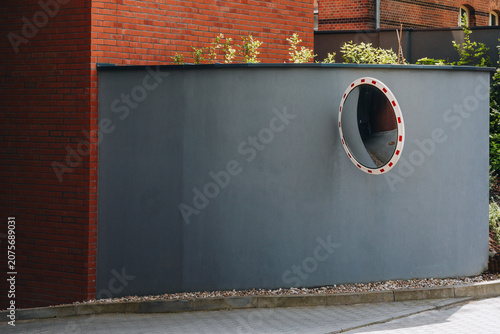 Convex traffic mirror mounted on gray concrete wall near red brick building