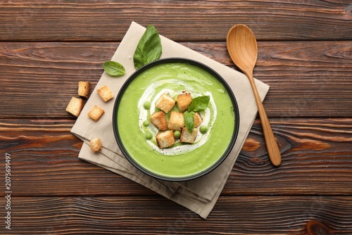 Foto Delicious pea cream soup served with basil and croutons on wooden table, flat la