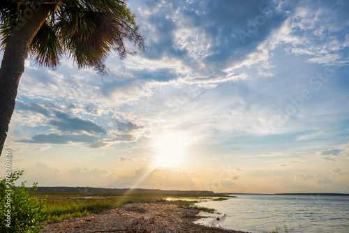 Sunset over the water with clouds and reflections in the sky near a riverbank