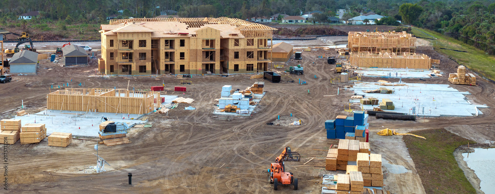 Naklejka premium Unfinished frames of apartment condos with wooden roofs under construction. Development of residential housing in US suburbs. Real estate market in the USA