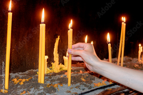 Fényképezés Hand lighting devotional candles inside a Christian church
