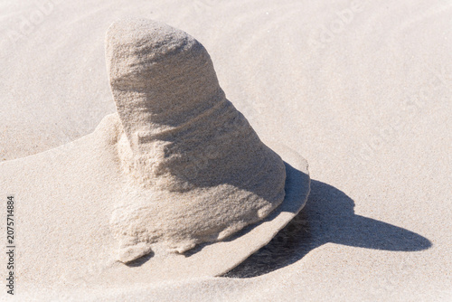 A sand structure resembling a cone, shaped by the wind, and placed on a flat sandy surface. Karwia beach. Karwia. Poland