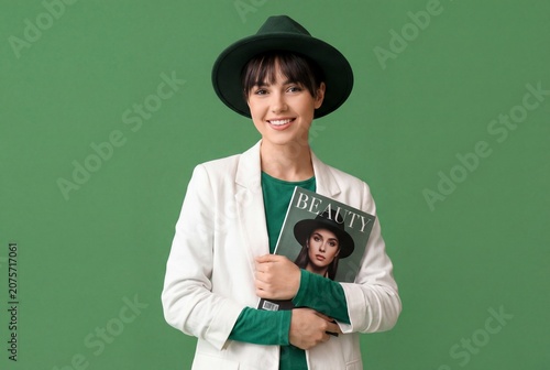 Stylish young woman in white blazer and green felt hat holding beauty magazine