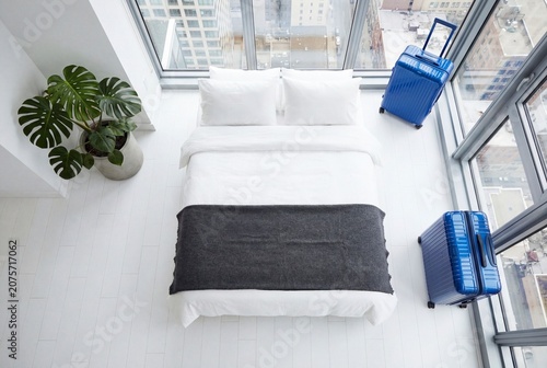 Modern minimalist bedroom with blue suitcases and city view through panoramic windows