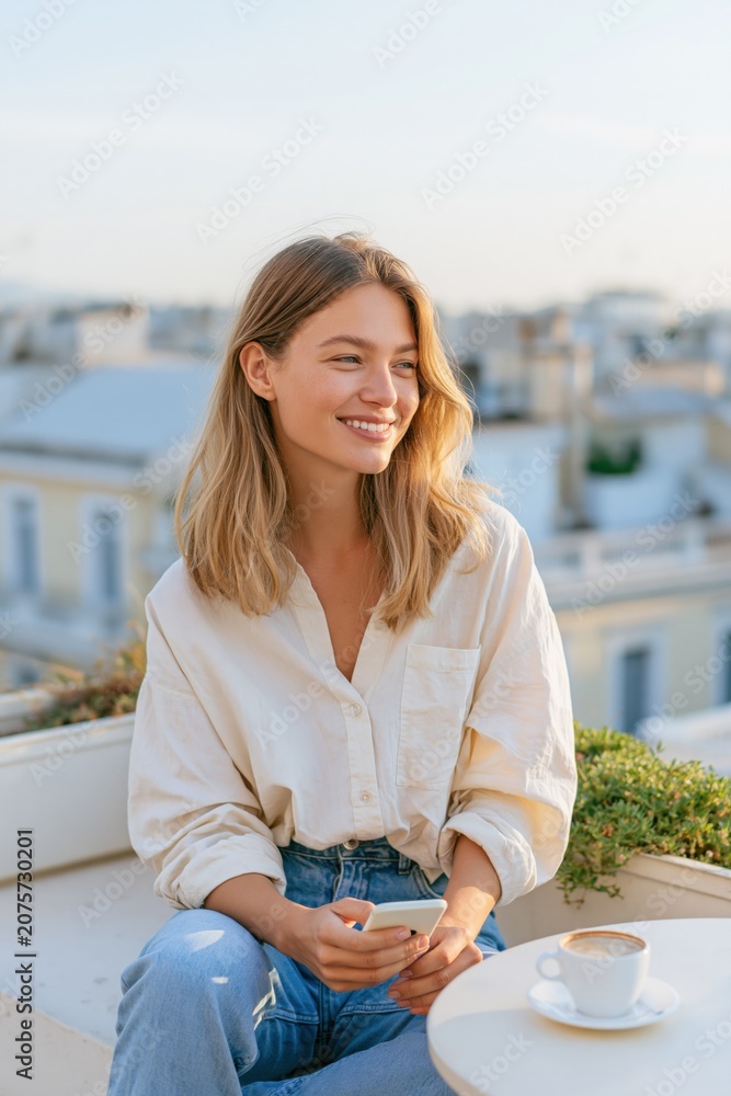 Fototapeta premium Young woman smiling on a rooftop terrace with coffee and smartphone for lifestyle banner and social media background
