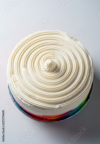 Top view of a circular gourmet cake featuring a thick, elegant layer of smooth white buttercream icing styled in a decorative swirl pattern, pattern, professional, frosting