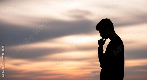 Silhouette of a thoughtful male figure against a soft sunset sky