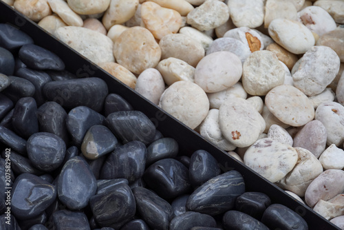 Contrast of smooth dark and light natural river stones arranged in a split background
