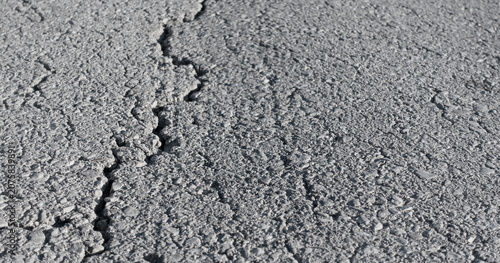 Cracked asphalt road surface. Damaged dark pavement with visible cracks