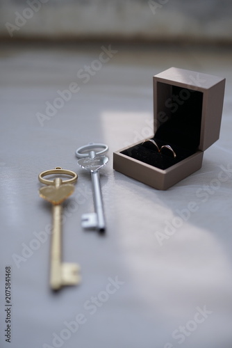 Golden and silver keys rest near an open ring box holding wedding bands, symbolizing deep love, partnership, and a new life chapter