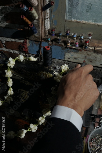 Artisan hand working on traditional machine with style floral decoration and sewing spools in shop