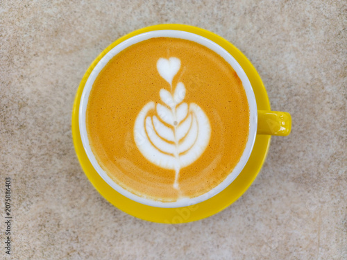 Coffee latte art with tulip pattern in yellow ceramic cup and saucer on textured table background. Hot cappuccino espresso beverage closeup view.