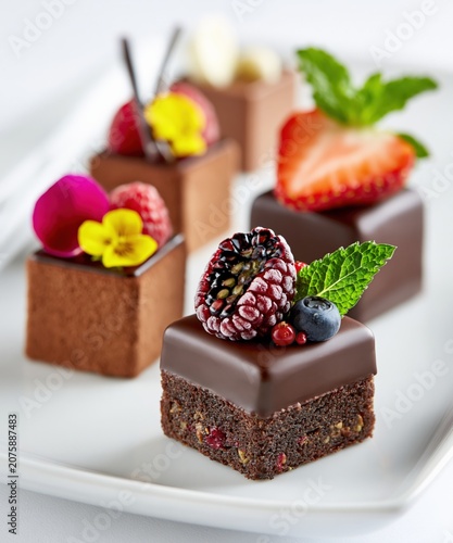 Gourmet chocolate petit fours adorned with fresh berries and mint, offering an elegant dessert experience