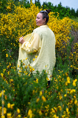 Obraz na płótnie Young woman in a flowing yellow kimono standing among bright yellow broom flowers at a forest edge glancing to the side