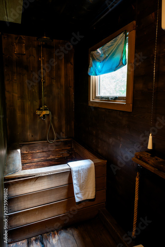 Fotografía Dark wooden Japanese-style soaking tub with a vintage brass rain shower in a rustic forest cabin bathroom