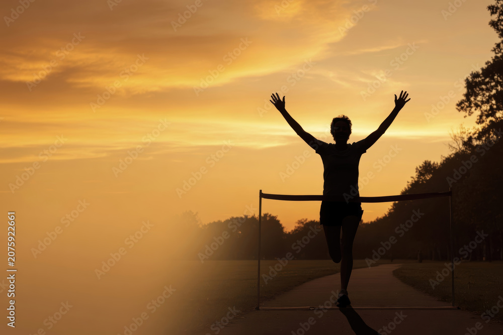 Fototapeta premium Runner sunset silhouette finish line victory success motivation sports outdoor fitness peaceful runner sunset silhouette finish line park, victory pose with raised arms, success and motivation