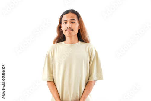 A studio portrait of a young Asian man with long, wavy brown hair and a mustache, wearing a plain beige t-shirt, looking directly at the camera.