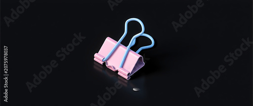 Close up of a pink and blue binder clip on a dark reflective floor.