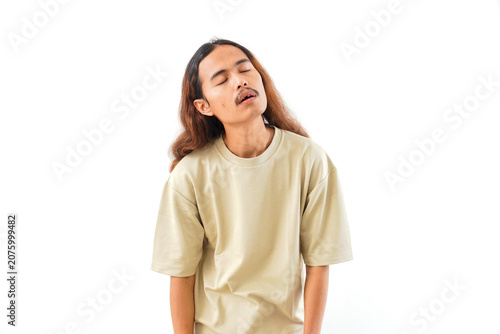 Fotografía A young man with long hair and a mustache, wearing a beige t-shirt, appears exhausted with his eyes closed and mouth slightly open, isolated on white