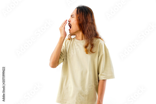A man with long hair and a mustache yawning while covering his mouth with his hand, captured in a studio portrait against a clean white background.