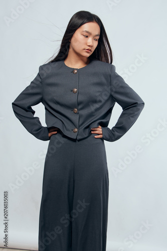Obraz na plátně Young woman with long dark hair posing in modern dark gray outfit with buttoned jacket and matching skirt on light background