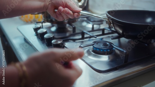 Foto Person adjusting gas flame on a modern stainless steel stovetop while holding a