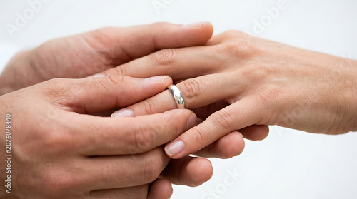 Groom putting silver wedding ring on bride's finger during marriage ceremony isolated on white background