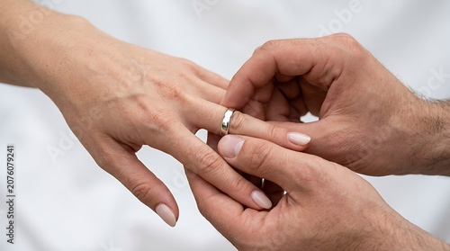 A close-up shot of a person placing a wedding ring on another person's finger, symbolizing commitment and love in a ceremony or proposal